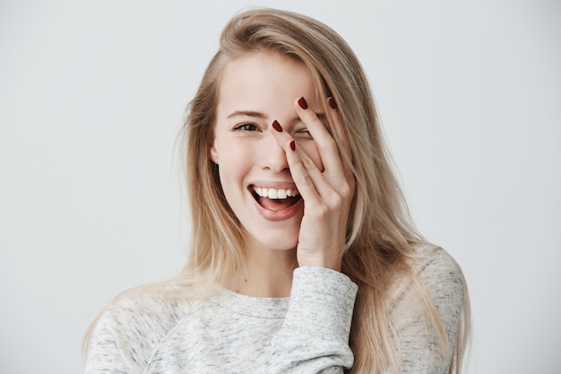 Headshot van leuke vrouw met donkere ogen, blond lang haar, gelukkige zachte glimlach die haar succes verheugen.