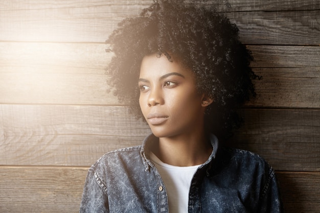 Headshot van modieuze jonge donkere vrouw met afro kapsel gekleed in denim jasje