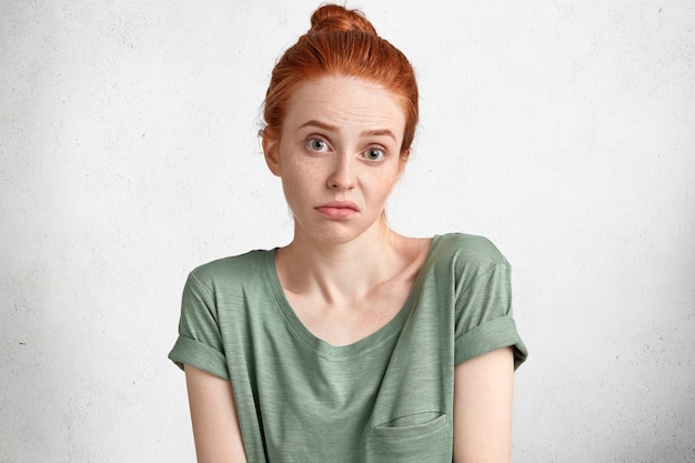 Gratis foto headshot van ontevredenheid onzekere twijfelachtige vrouw met rood haar vastgebonden in knot, aarzelt ergens over, ontevreden zijn met alles poseert tegen wit