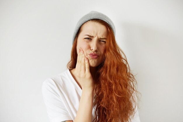 Headshot van roodharige tienervrouw die met pijnlijke uitdrukking op haar wang drukt