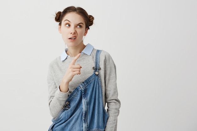 Headshot van uitdagende vrouwenjaren '20 die wijsvinger zijwaarts op iets met fronsend gezicht richten. Jonge vrouw met sceptische blik aan kant het gesturing uitdrukken van wantrouwen. Lichaamstaal