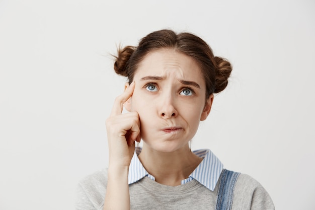 Headshot van volwassen meisje opzoeken met frons uiting geven aan misverstand. leuke vrouwelijke student die mond verdraait die haar schema probeert te herinneren of zich over examens hindert.