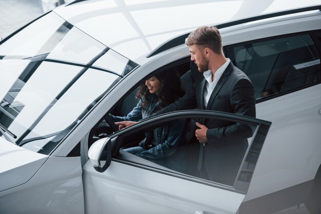 Heel interessant. Vrouwelijke klant en moderne stijlvolle bebaarde zakenman in de auto-salon