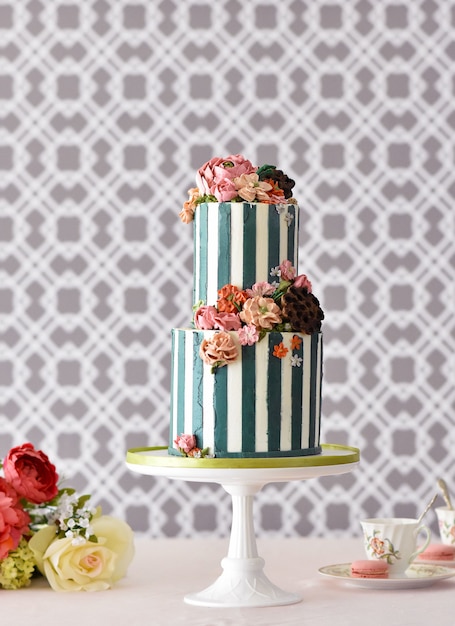 Heerlijke cake op twee niveaus met de decoratie van kleurrijke bloemen op een witte standaard