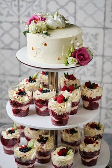 Heerlijke en mooie bruiloft set van kleinigheden en cake. de witte taart is gedecoreerd met natuurlijke roze bloemen. cupcakes zijn versierd met verse bessen en bloemen.