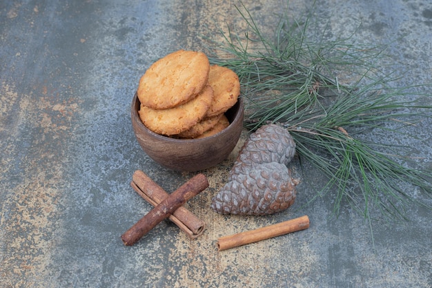 Gratis foto heerlijke koekjes op houten kom met kaneelstokjes en dennenappels op marmeren tafel.