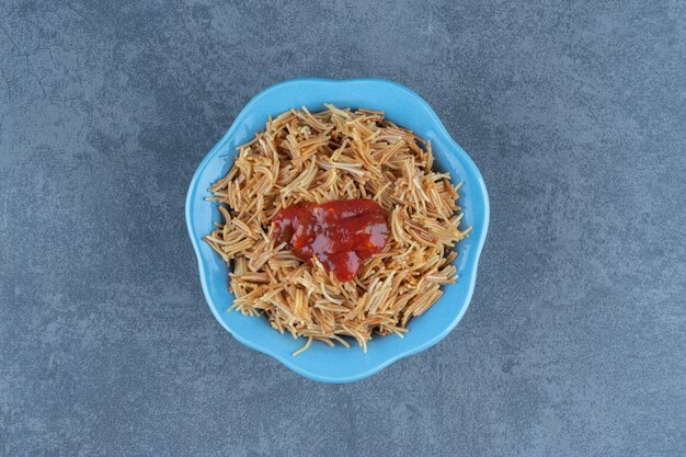 Heerlijke macaroni met ketchup in blauwe kom.