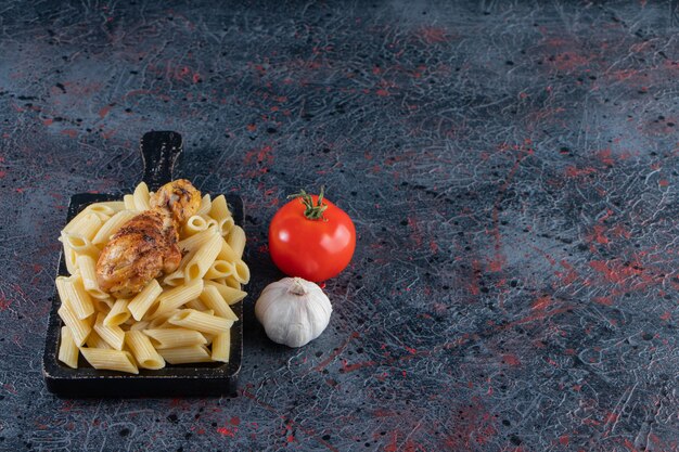Heerlijke penne pasta en kippenpoot op zwarte snijplank.
