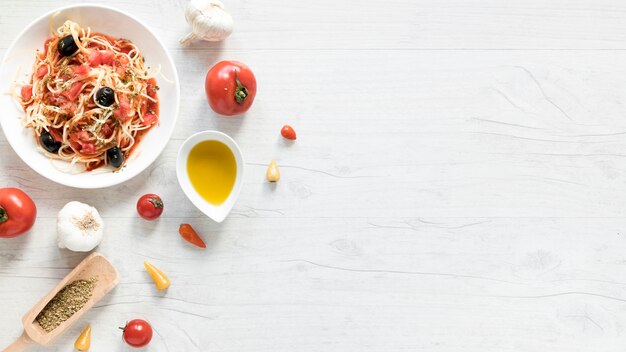 Heerlijke spaghettideegwaren op plaat; verse tomaat; kom met olijfolie en kruiden op houten bureau