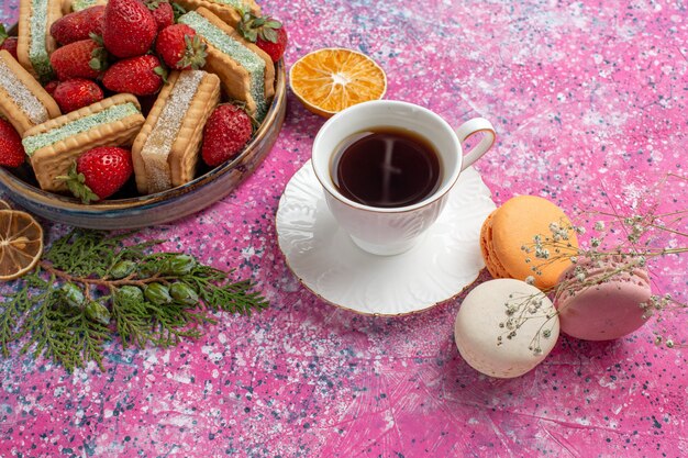 Heerlijke wafelsandwiches met kopje thee, macarons en verse rode aardbeien