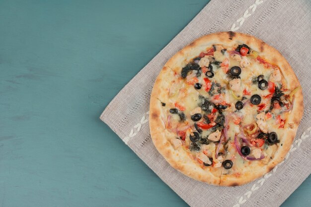 Heerlijke warme pizza met olijven en tomaten op blauwe tafel.