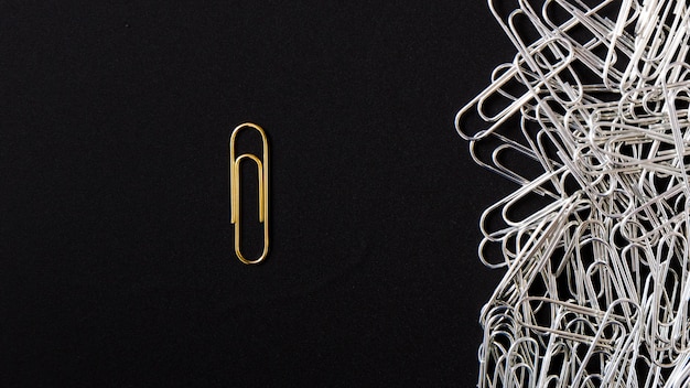 Heldere gouden paperclip die van zilveren klemmen op zwarte achtergrond duidelijk uitkomt