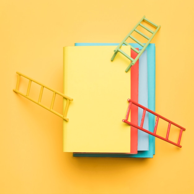 Heldere ladders op stapel kleurrijke lege boeken op gele achtergrond