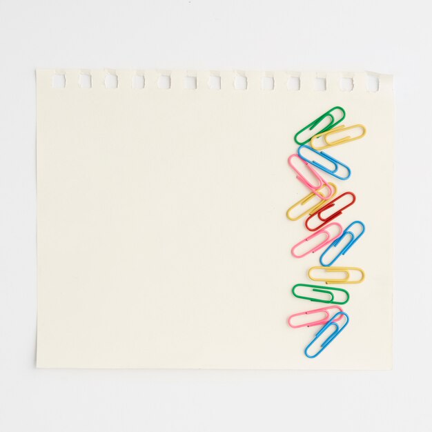 Heldere veelkleurige paperclips op papier tegen witte achtergrond