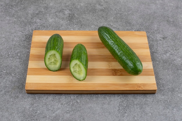 Hele of half gesneden komkommers op een houten bord over grijs oppervlak