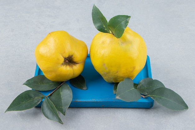 Hele rijpe kweeperen met bladeren op blauw bord