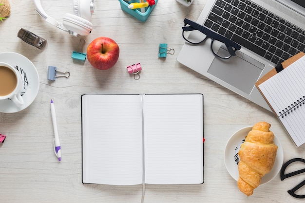 Gratis foto hele rode appel; croissant en theekop met bureaulevering en laptop op houten lijst