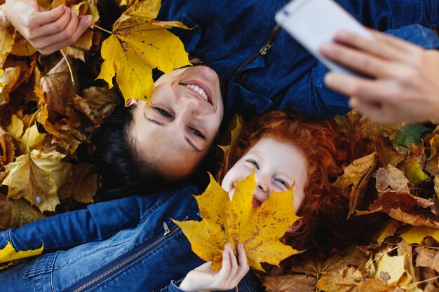 Herfstvibe, familieportret. Charmante moeder en haar dochter met rood haar hebben plezier bij het nemen van een selfie op sm