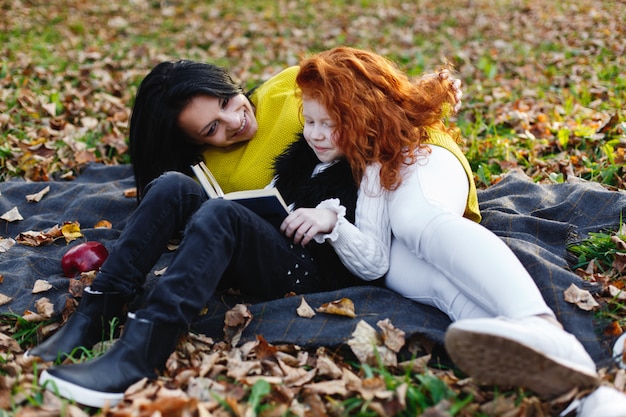 Gratis foto herfstvibe, familieportret. charmante moeder en haar dochter met rood haar hebben veel plezier op de gevallenen