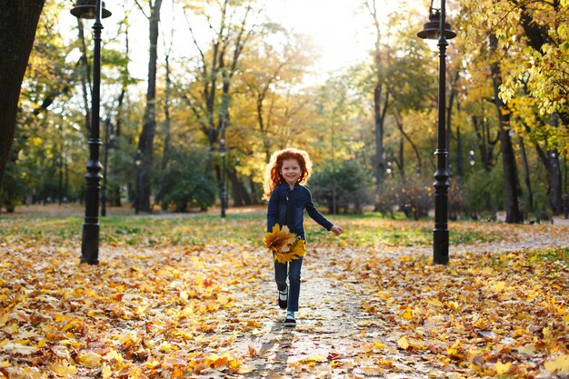 Herfstvibe, kindportret. Het charmante en rode haarmeisje kijkt gelukkig lopend en spelend op t