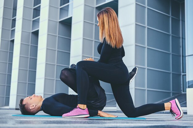 Het atletische fitnesspaar oefent op een aerobe mat over de achtergrond van een modern gebouw.