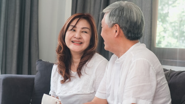 Het aziatische hogere paar ontspant thuis. aziatische hogere chinese grootouders, echtgenoot en vrouwen gelukkige glimlachomhelzing die samen terwijl thuis het liggen op bank in woonkamerconcept spreken.