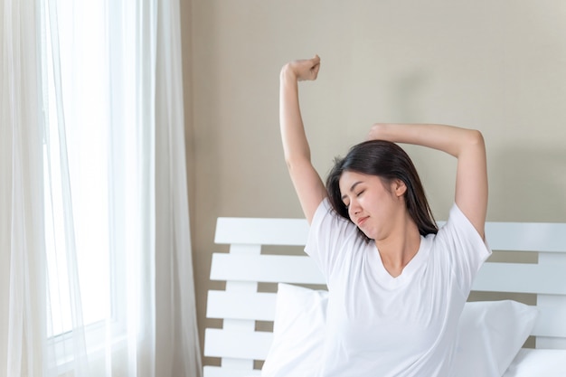 Het Aziatische jonge mooie vrouw uitrekken zich in bed na kielzog omhoog in de ochtend