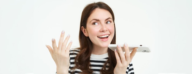 Het beeld van een schattige brunette vrouw die in de luidspreker praat en een mobiele telefoon bij de mond houdt, neemt haar op