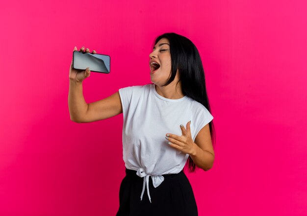 Het blije jonge Kaukasische meisje houdt telefoon die beweert te zingen