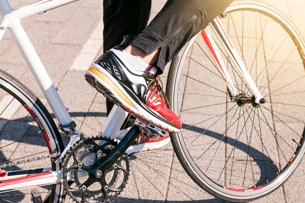 Het close-up van mannetje die jeans dragen en sportschoenen dragen berijdt fiets op het park