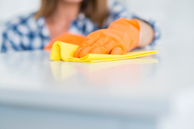 Het close-up van vrouw die handschoenen draagt ​​veegt het witte bureau met geel servet af