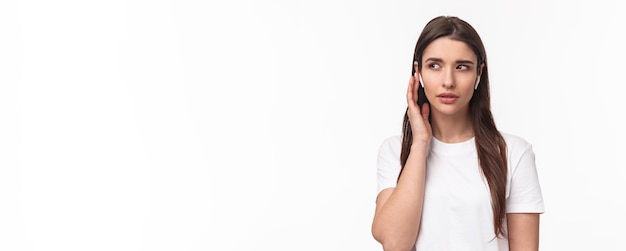 Het close-upportret van een jonge blanke vrouw in een t-shirt met een draadloze hoofdtelefoon luistert nauwgezet