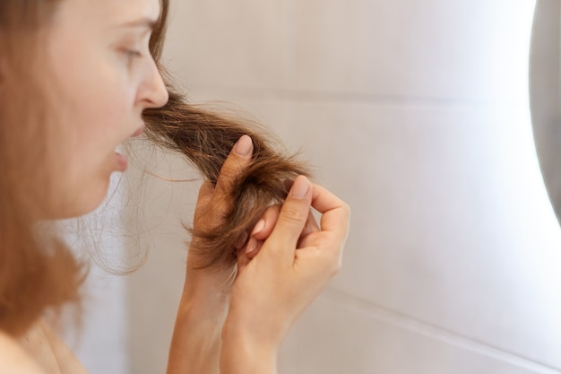 Het close-upprofielportret van verstoorde verbaasde vrouw die haar droog haar bekijkt, problemen heeft, moet shampoo of speciale behandeling bij trichologische kliniek veranderen.