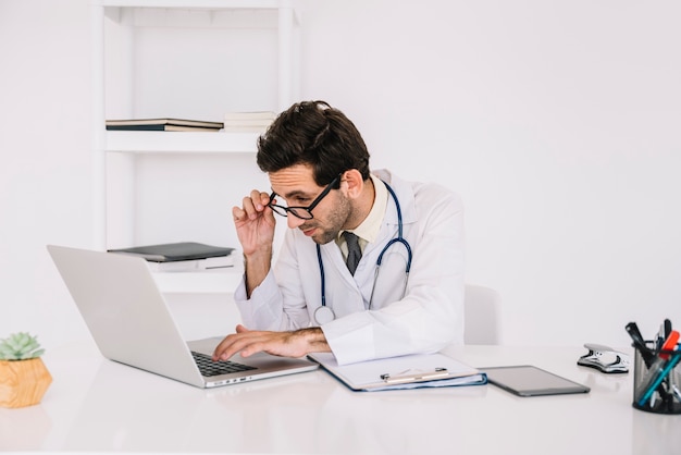 Het concentreren van jonge mannelijke arts die aan laptop in kliniek werkt