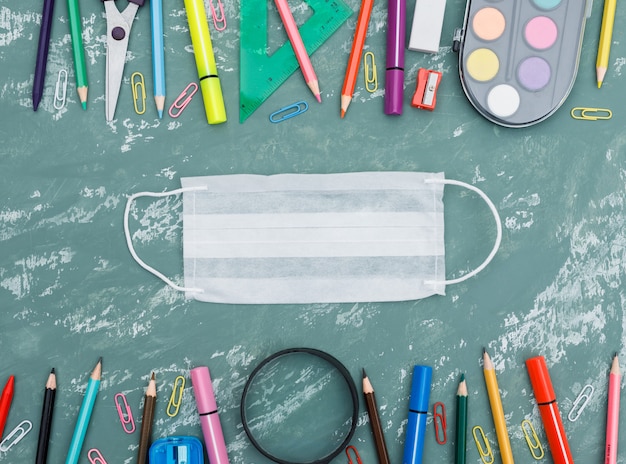 Het concept van de schoolquarantaine met medisch masker, vergrootglas, schoollevering op pleister achtergrondvlakte lag.