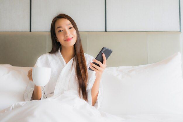 Het gebruik slimme mobiele telefoon van de portret mooie jonge Aziatische vrouw in slaapkamer