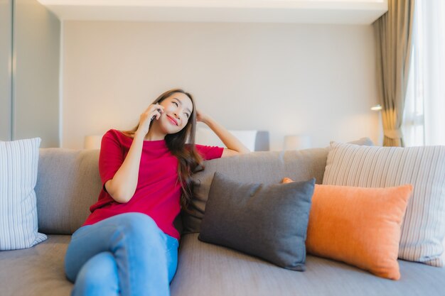 Het gebruik slimme mobiele telefoon van de portret mooie jonge Aziatische vrouw op bank