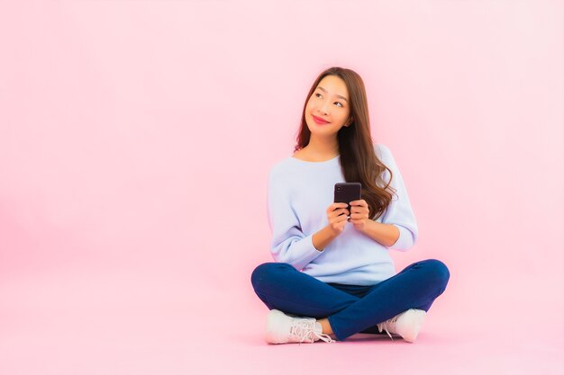 Het gebruik van de portret mooie jonge Aziatische vrouw slimme mobiele telefoon op roze kleur geïsoleerde muur