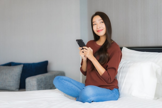 Het gebruik van slimme mobiele telefoon van de portret mooie jonge aziatische vrouw op bed in slaapkamerbinnenland