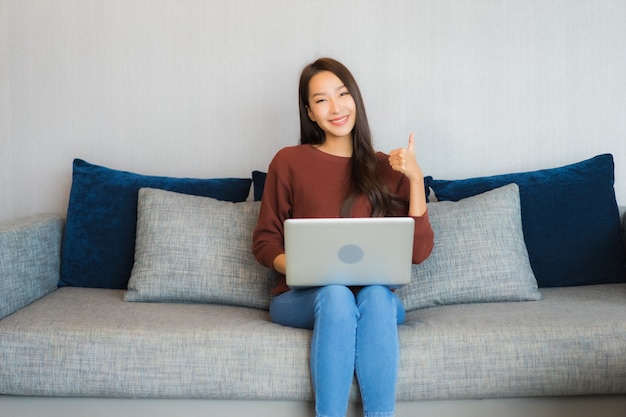 Het gebruikcomputerlaptop van de portret mooie jonge Aziatische vrouw op bank in woonkamerbinnenland