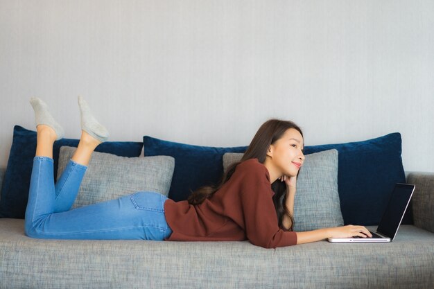 Het gebruikcomputerlaptop van de portret mooie jonge Aziatische vrouw op bank in woonkamerbinnenland