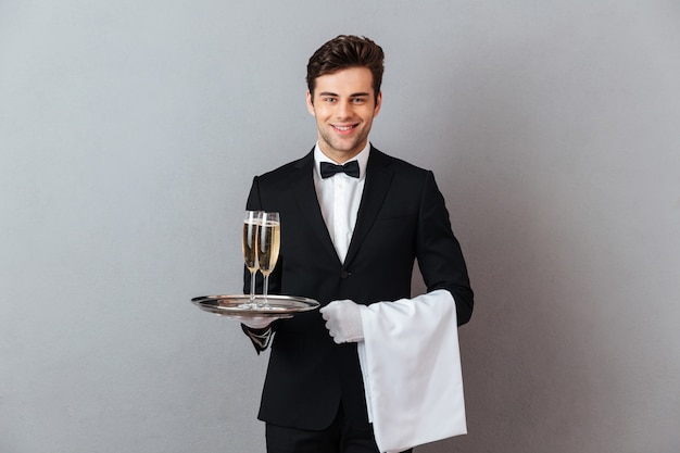 Gratis foto het gelukkige jonge glas van de kelnersholding champagne en handdoek.