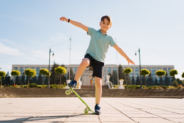 Het gelukkige jonge jongen spelen op skateboard in het park, Kaukasisch jong geitje die stuiverraad berijden, die skateboard uitoefenen.