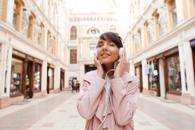 Het gelukkige jonge vrouw genieten die aan muziek op een stadsstraat luisteren