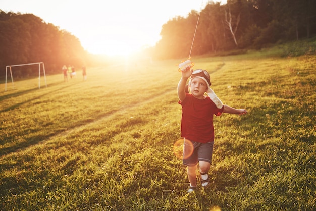 Het gelukkige kind lanceert een vlieger in het gebied bij zonsondergang. Kleine jongen en meisje op zomervakantie