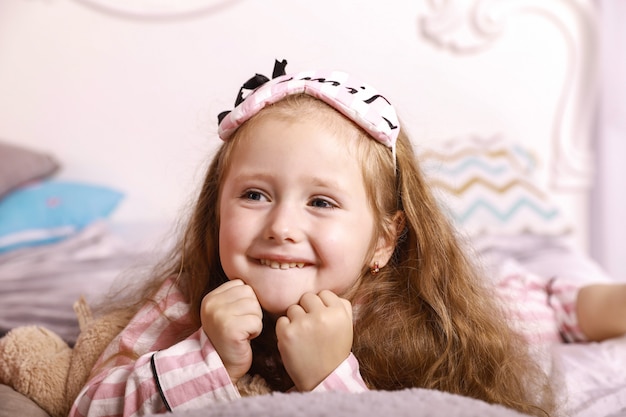 Het gelukkige kind van het glimlachen roodharige meisje ligt op de lakens op het reusachtige bed gekleed in roze pyjama