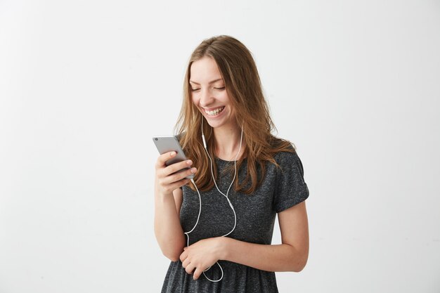 Het gelukkige vrolijke meisje glimlachen die het telefoonscherm bekijken die aan streaming muziek luisteren.