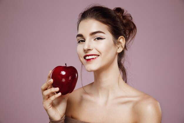 Het gelukkige vrouw glimlachen die rode appel op roze houdt