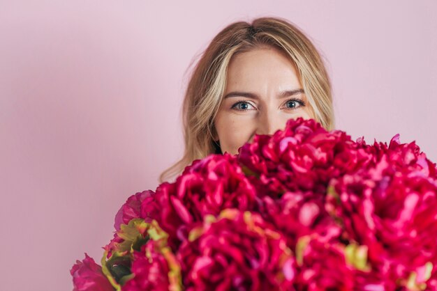 Het gezicht van de jonge vrouw achter het mooie rozenboeket tegen roze achtergrond