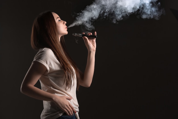 Het gezicht van de jonge vrouw vapen in zwarte studio